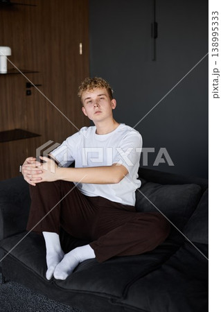 Young man with white skin relaxes on dark sofa in living room Young man with white skin relaxes on dark sofa in living room 138995333