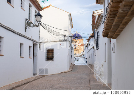 Winding cobblestone street in Altea, Spain, featuring traditional whitewashed houses and the iconic blue-domed church visible in the distance, a perfect setting for family holidays and tourism during 138995953