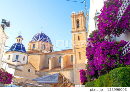 Sunny Altea old town street scene with the famous blue tiled church dome and bell tower framed by abundant purple bougainvillea, perfect for a Spanish holiday Sunny Altea old town street scene with the famous blue tiled church dome and bell tower framed by abundant purple bougainvillea, perfect for a Spanish holiday 138996008