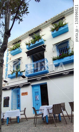 Traditional white building with vibrant blue details and outdoor restaurant seating in Altea, Spain, offering a welcoming scene for travelers Traditional white building with vibrant blue details and outdoor restaurant seating in Altea, Spain, offering a welcoming scene for travelers 138996021