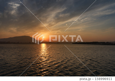 山のシルエットと雲が広がる空の下、海面に反射する黄金色の夕日 山のシルエットと雲が広がる空の下、海面に反射する黄金色の夕日 138996911