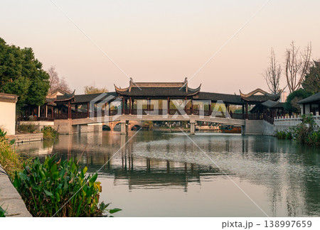 Luzhi, China - December 10, 2017: Elegant covered bridge with traditional Chinese architecture gracefully spans a tranquil waterway in a historic water town Luzhi, China - December 10, 2017: Elegant covered bridge with traditional Chinese architecture gracefully spans a tranquil waterway in a historic water town 138997659