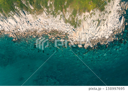 Rugged rocky coastline meets clear turquoise ocean waters, revealing underwater formations and green vegetation from an aerial view Rugged rocky coastline meets clear turquoise ocean waters, revealing underwater formations and green vegetation from an aerial view 138997695