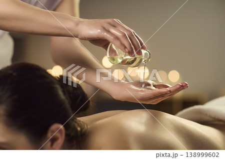 Aromatherapy massage with oil pour on back in spa, warm candles and relaxing care Aromatherapy massage with oil pour on back in spa, warm candles and relaxing care 138999602
