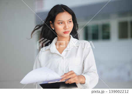 Confident young businesswoman holding a report clipboard in a modern office setting. Professional female manager looking ahead with focus, representing leadership, planning, and corporate success. Confident young businesswoman holding a report clipboard in a modern office setting. Professional female manager looking ahead with focus, representing leadership, planning, and corporate success. 139002212