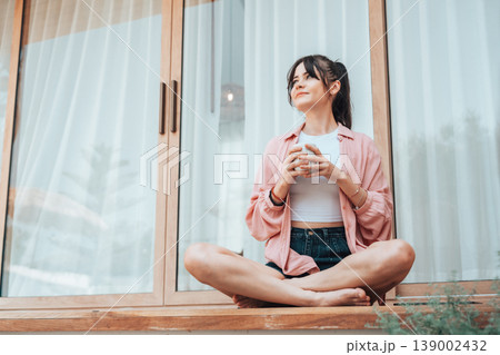Young woman relaxing on a terrace at home, holding a cup and enjoying a calm moment Young woman relaxing on a terrace at home, holding a cup and enjoying a calm moment 139002432