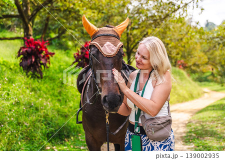 Young woman gently stroking horse in tropical garden, emotional connection with animal during outdoor activity Young woman gently stroking horse in tropical garden, emotional connection with animal during outdoor activity 139002935