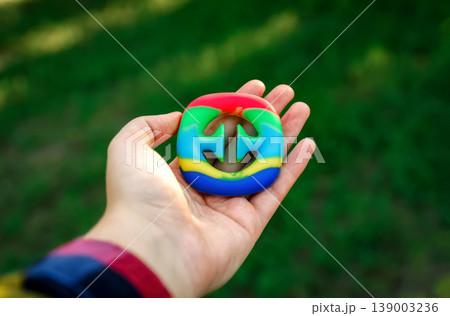 Close-up of a hand holding a colorful rainbow silicone snapper fidget toy. Sensory anti-stress toy for kids and adults on a blurred green nature background 139003236