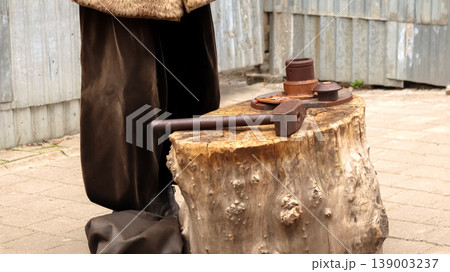 Close-up of a large old hammer lying on a tree stump anvil. Historical reenactment of traditional coin minting or blacksmithing outdoors. Craftsmans tools on a wooden block Close-up of a large old hammer lying on a tree stump anvil. Historical reenactment of traditional coin minting or blacksmithing outdoors. Craftsmans tools on a wooden block 139003237