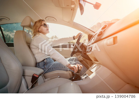 Woman Car Driving Sunlit Interior - A woman in sunglasses drives a car on a sunny day. The sun illuminates the car's interior. 139004786
