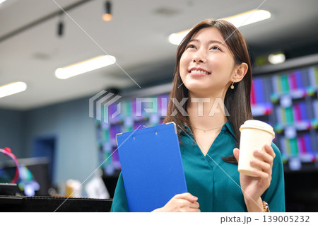 オフィスで笑顔で上を見上げるビジネスパーソンの女性 クリップボードとコーヒーを持つ オフィスで笑顔で上を見上げるビジネスパーソンの女性 クリップボードとコーヒーを持つ 139005232