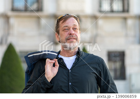 Man about 55 years old holding jacket on shoulder looking aside outdoors Man about 55 years old holding jacket on shoulder looking aside outdoors 139006859