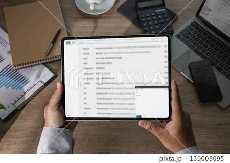 Hands holding tablet with email inbox beside laptop, phone, calculator, and documents on desk, representing business communication, message handling, digital correspondence, and office workflow Hands holding tablet with email inbox beside laptop, phone, calculator, and documents on desk, representing business communication, message handling, digital correspondence, and office workflow 139008095