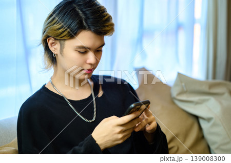 ソファでリラックスしながらスマートフォンを操作するスタイリッシュな若い男性 ソファでリラックスしながらスマートフォンを操作するスタイリッシュな若い男性 139008300