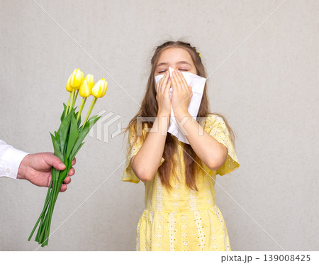 Young girl sneezing into tissue while offered yellow tulip flower during allergy season Young girl sneezing into tissue while offered yellow tulip flower during allergy season 139008425