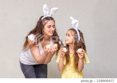 Mother and daughter wearing bunny ears holding Easter eggs and sharing a joyful spring moment Mother and daughter wearing bunny ears holding Easter eggs and sharing a joyful spring moment 139008427