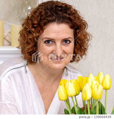 Smiling middle-aged woman holding yellow tulips in a warm home portrait with natural light Smiling middle-aged woman holding yellow tulips in a warm home portrait with natural light 139008439