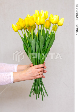 Woman holding a bouquet of yellow tulip blooms against a neutral background Woman holding a bouquet of yellow tulip blooms against a neutral background 139008440