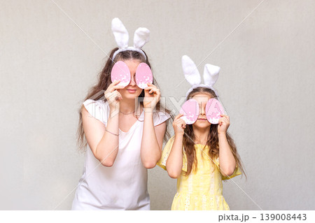 Mother and daughter wearing bunny ears holding pink Easter egg masks over their eyes Mother and daughter wearing bunny ears holding pink Easter egg masks over their eyes 139008443