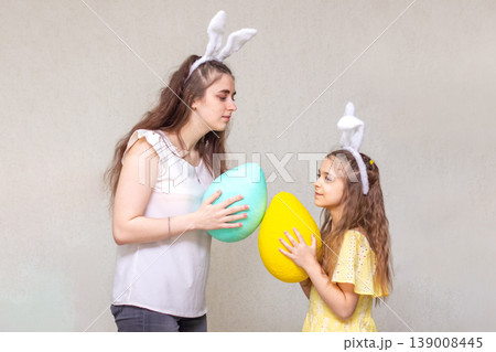 Mother and daughter wearing bunny ears sharing large colorful Easter eggs and playful spring moments Mother and daughter wearing bunny ears sharing large colorful Easter eggs and playful spring moments 139008445