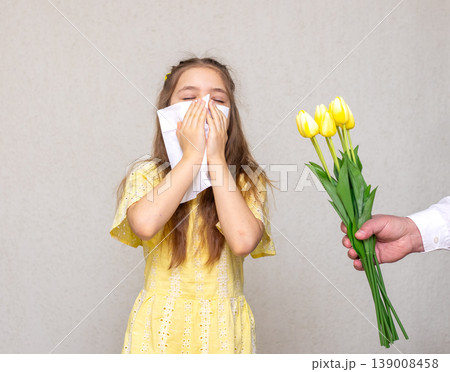 Young girl sneezing into a tissue as a hand offers a yellow tulip causing an allergic reaction 139008458
