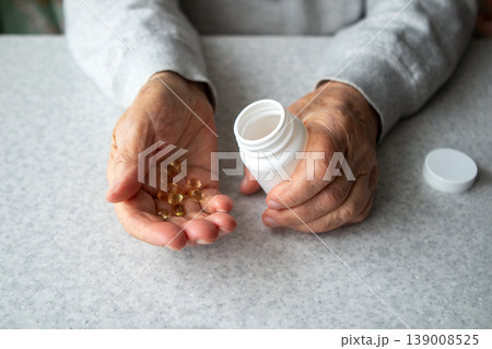 Elderly hands holding vitamin softgel pill from a white medicine bottle on countertop Elderly hands holding vitamin softgel pill from a white medicine bottle on countertop 139008525
