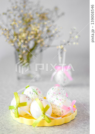 Decorative pastel Easter eggs with ribbon bows on a yellow tray and blurred floral background Decorative pastel Easter eggs with ribbon bows on a yellow tray and blurred floral background 139008546