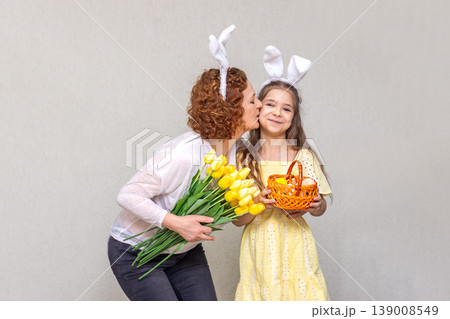 Mother kisses daughter wearing bunny ears while holding tulip bouquet and Easter basket Mother kisses daughter wearing bunny ears while holding tulip bouquet and Easter basket 139008549