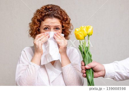Woman sneezing into tissue after receiving a yellow tulip bouquet showing allergic reaction Woman sneezing into tissue after receiving a yellow tulip bouquet showing allergic reaction 139008598
