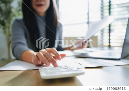Focused woman calculates figures at desk Focused woman calculates figures at desk 139008618