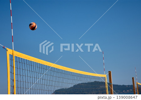 Volleyball in the air over a yellow net during a beach match in Baiona under a clear blue sky Volleyball in the air over a yellow net during a beach match in Baiona under a clear blue sky 139008647