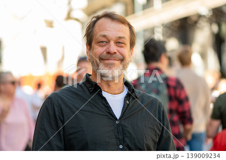 Man age 50-55 smiling on city street among people Man age 50-55 smiling on city street among people 139009234