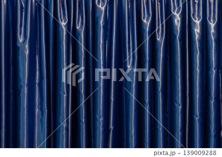 Blue curtain with glossy surface forming vertical folds in interior Blue curtain with glossy surface forming vertical folds in interior 139009288
