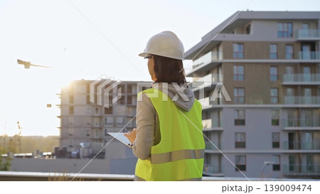 Woman construction engineer is taking notes with a tablet pc while inspecting a construction site in the morning at sunrise Woman construction engineer is taking notes with a tablet pc while inspecting a construction site in the morning at sunrise 139009474