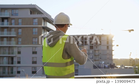 Man constructive engineer with white hard hat and safety vest is using a tablet computer while inspecting a construction site at sunset Man constructive engineer with white hard hat and safety vest is using a tablet computer while inspecting a construction site at sunset 139009475