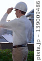 Man a constructive engineer wearing white shirt and hard hat is making notes on a clipboard while inspecting a building site at sunrise, back and vertical view . Architect at work 139009486