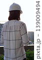 Female construction engineer wearing white checked blouse and hard hat is using tablet computer while inspecting a building site at sunset, back and vertical view. Architecture concept 139009494