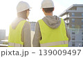 Two architects wearing safety hard hats and vests holding blueprint and discussing construction site project at sunrise, back view. Architecture, engineering and teamwork concept 139009497