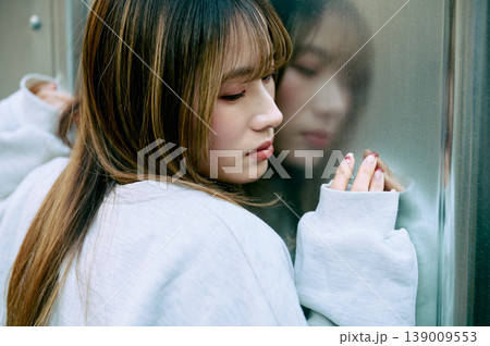 窓に映る自分の姿をアンニュイな表情で見つめる若い女性のポートレート 窓に映る自分の姿をアンニュイな表情で見つめる若い女性のポートレート 139009553