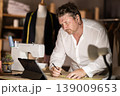 Middle-aged male dressmaker drawing on paper watching video-course 139009653