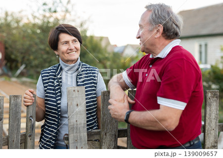 Positive mature man and woman standing near fence in garden Positive mature man and woman standing near fence in garden 139009657