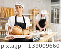 Female baker with basket of aromatic baguettes in bakery 139009660