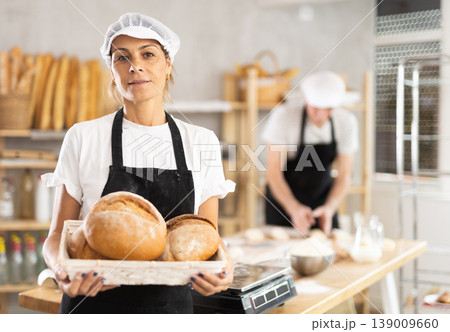 Female baker with basket of aromatic baguettes in bakery 139009660