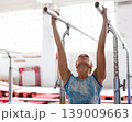 Woman gymnast performs complex acrobatic exercise on parallel bars in gym 139009663