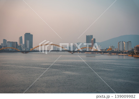 Dragon bridge over calm Han river at sunset with soft golden light and peaceful city skyline of Da Nang, tranquil urban landscape with serene water and warm evening atmosphere, Danang Vietnam Dragon bridge over calm Han river at sunset with soft golden light and peaceful city skyline of Da Nang, tranquil urban landscape with serene water and warm evening atmosphere, Danang Vietnam 139009982