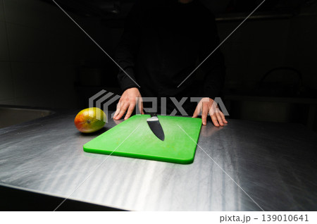 Chef preparing mango on green cutting board with knife in kitchen 139010641