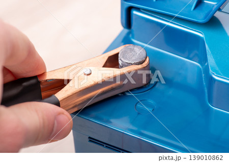 Blue car accumulator battery and cleat in male`s hand on a white background, close up. Concept of service, maintenance, charging car battery Blue car accumulator battery and cleat in male`s hand on a white background, close up. Concept of service, maintenance, charging car battery 139010862