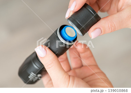 Female holding flashlight with 18650 battery, close up. Maintenance of portable pocket device for lighting darkness Female holding flashlight with 18650 battery, close up. Maintenance of portable pocket device for lighting darkness 139010868