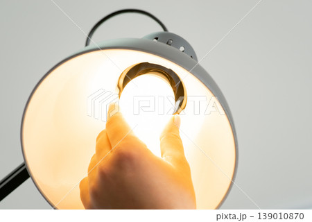 Close up shot of shining light bulb in the lamp, woman's hand changing it. Concept of convenient work, good conditions, modern interior, lightening the workplace 139010870