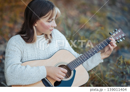 Girl playing the guitar. Portrait of a young girl playing the guitar outdoors, mastering her skills Girl playing the guitar. Portrait of a young girl playing the guitar outdoors, mastering her skills 139011404
